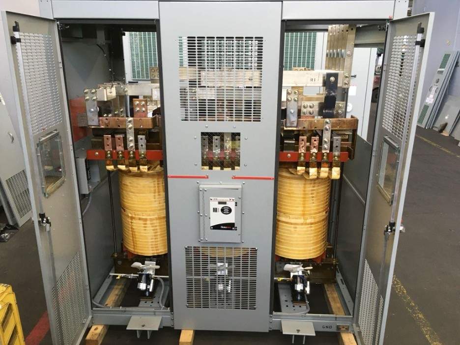 Industrial transformer with dual yellow coils, electrical components, and control panels demonstrating transformer