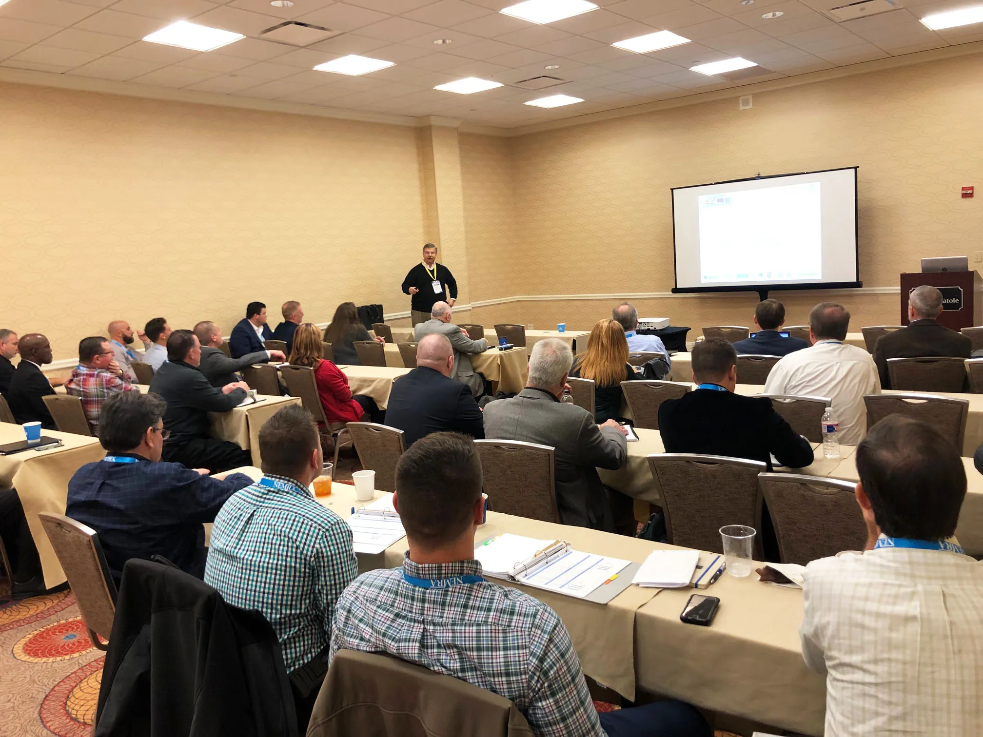 Speaker addresses audience at NEMRA 2019 conference in lecture hall with projection screen