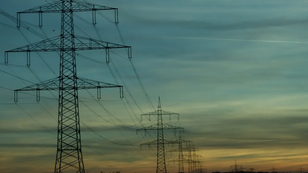 High-voltage transmission towers and power lines extending across horizon at sunset, representing electrical infrastructure