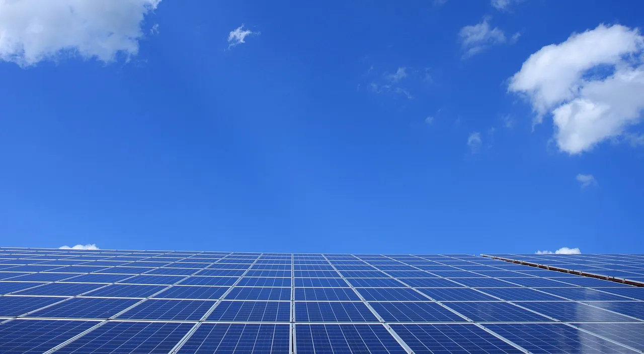 Solar panel array stretching across rooftop under clear blue sky with white clouds