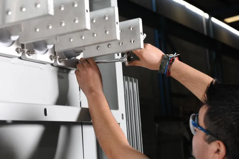 Technician installing aluminum mounting bracket with screwdriver on industrial equipment