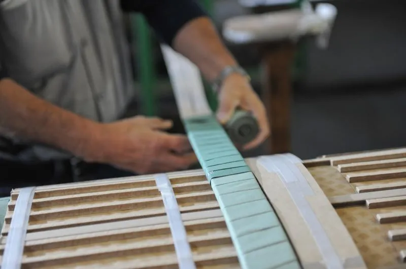 Craftsman installing turquoise fretboard on wooden guitar neck with precise hand placement