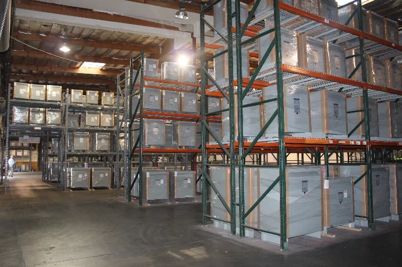 Industrial warehouse with tall green and orange pallet racking systems stacked with gray storage containers and cardboard
