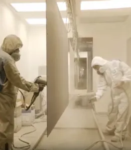 Workers in protective suits applying powder coating paint process in industrial facility