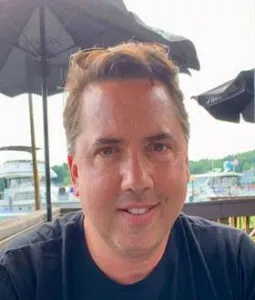 James Gibson smiling outdoors with umbrellas and waterfront in background