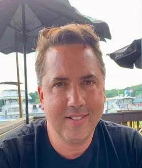 James Gibson smiling outdoors with umbrellas and waterfront in background