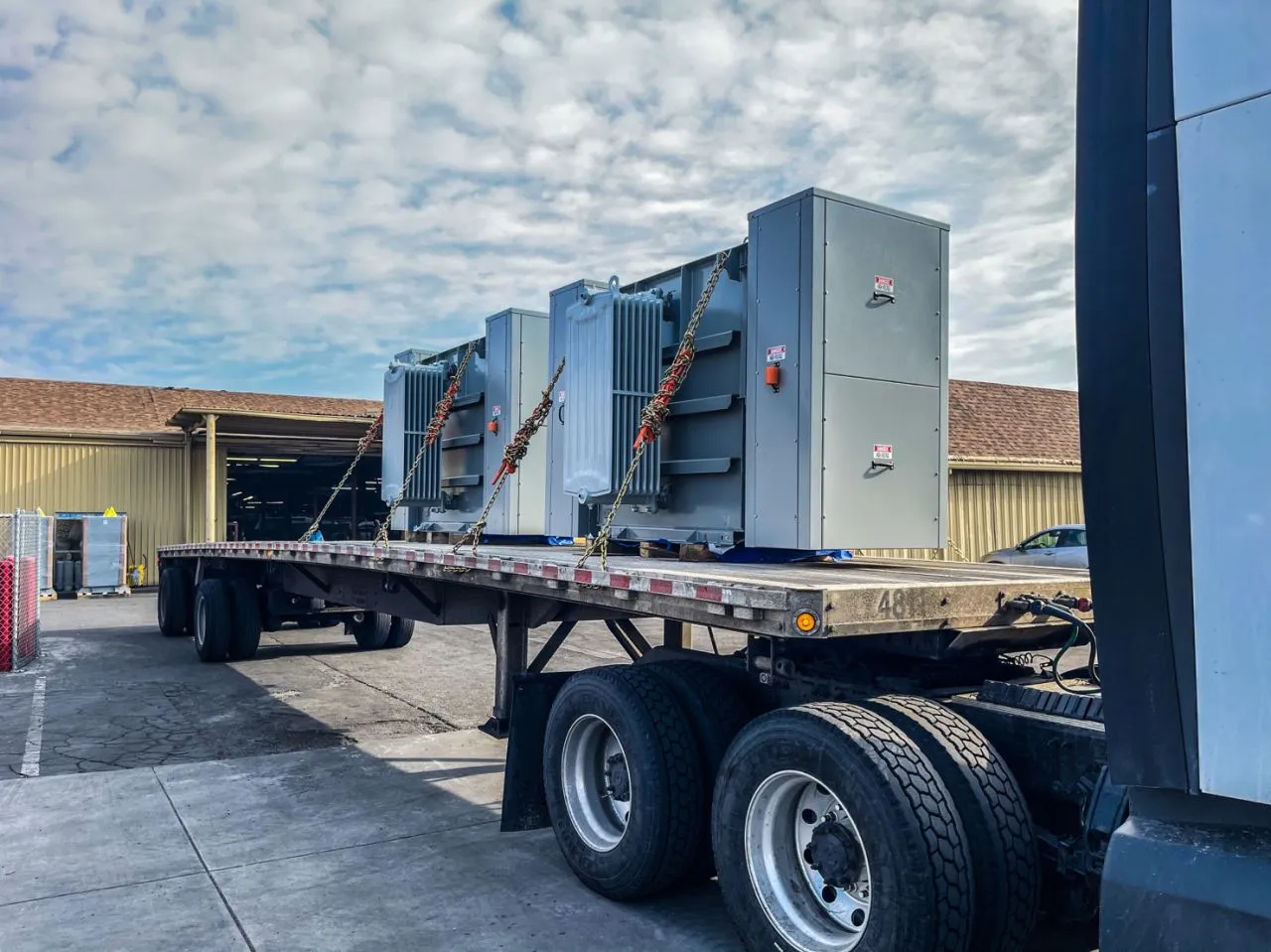 Industrial power transformers secured on flatbed trailer outside manufacturing facility