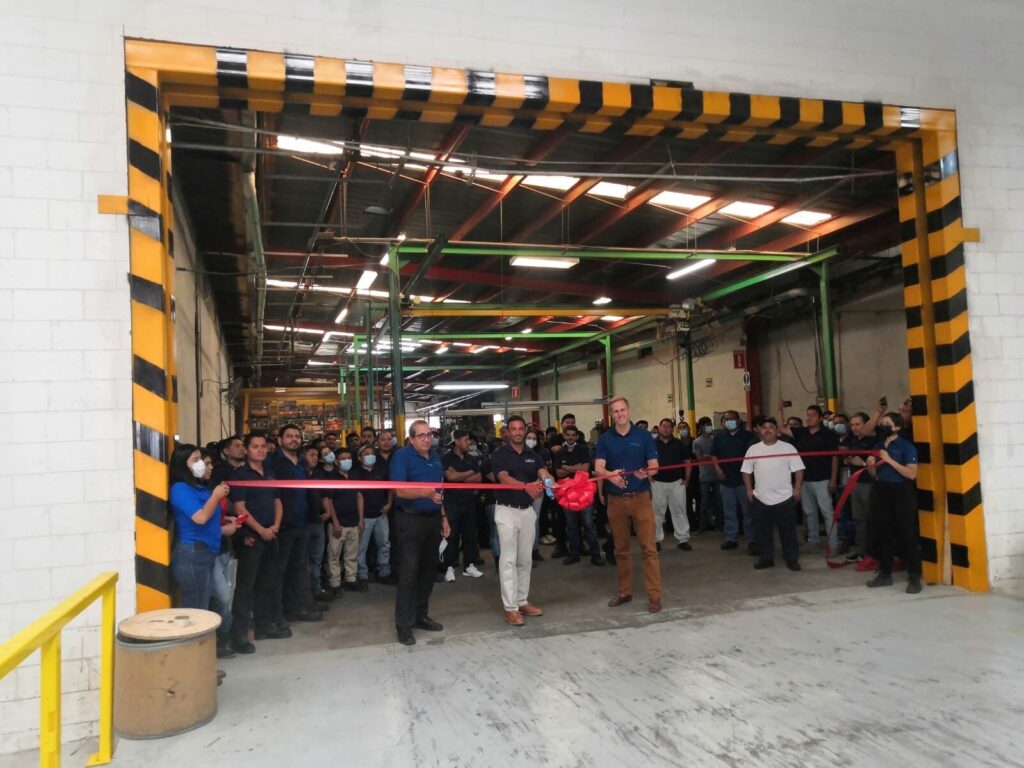 Group of people at ribbon cutting ceremony inside industrial facility with yellow and black striped entrance frame