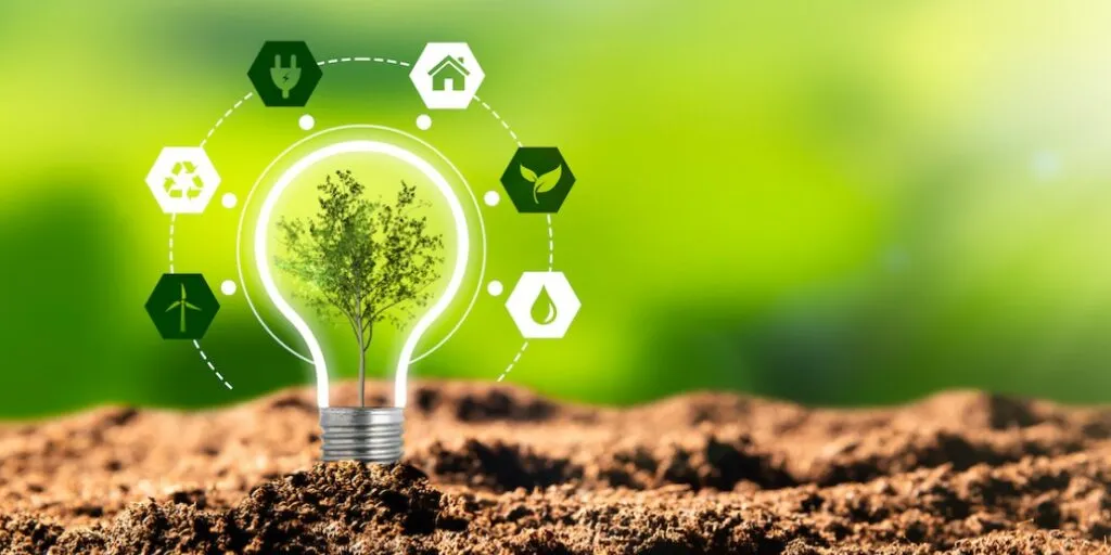 Light bulb with tree growing inside surrounded by renewable energy icons on soil with green background, representing