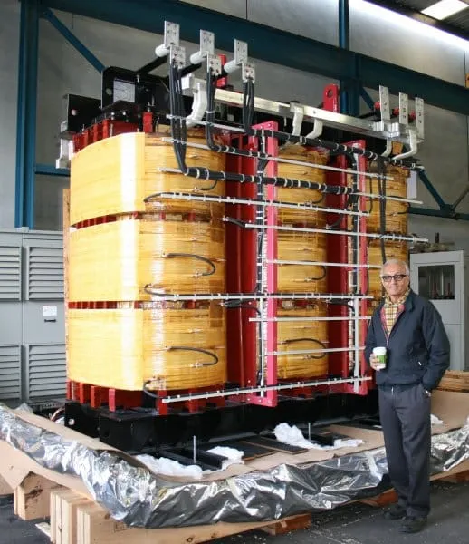 Man standing next to large yellow and red industrial transformer unit in factory setting