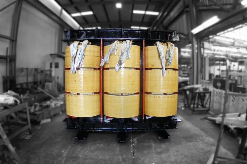 Three-phase industrial transformer with yellow coils in manufacturing facility warehouse