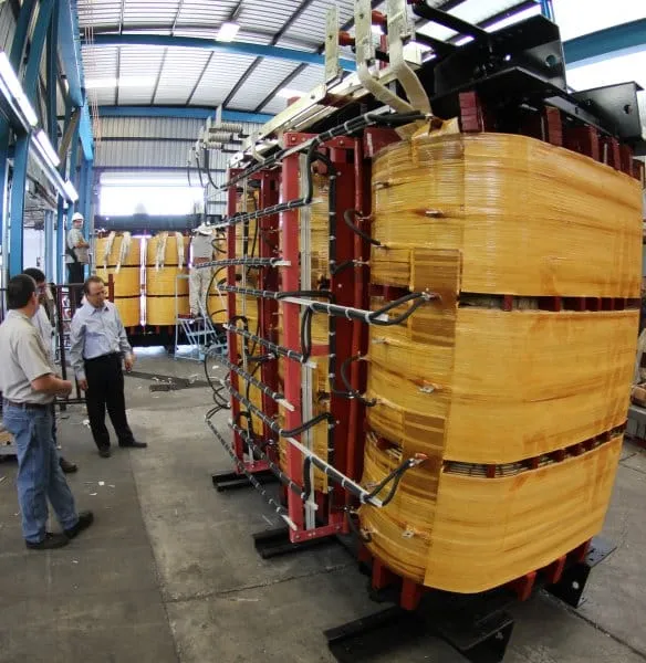 Industrial power transformer with red coils and yellow cylindrical tank in manufacturing facility warehouse