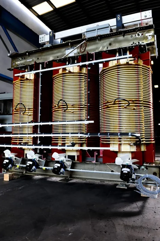 Large industrial power transformer with copper coils and red frame in manufacturing facility