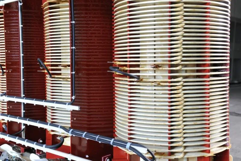 Stacked transformer coils with red and cream colored windings and metal cooling fins in industrial manufacturing facility