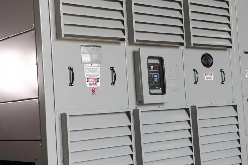 Industrial electrical panel with louvered vents, handles, and digital control display unit mounted on white cabinet doors