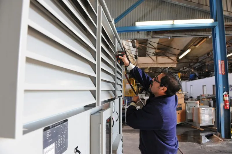 Technician installing white louvered panel on industrial equipment in manufacturing facility