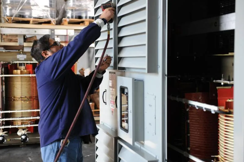 Technician installing transformer equipment on industrial electrical panel in manufacturing facility