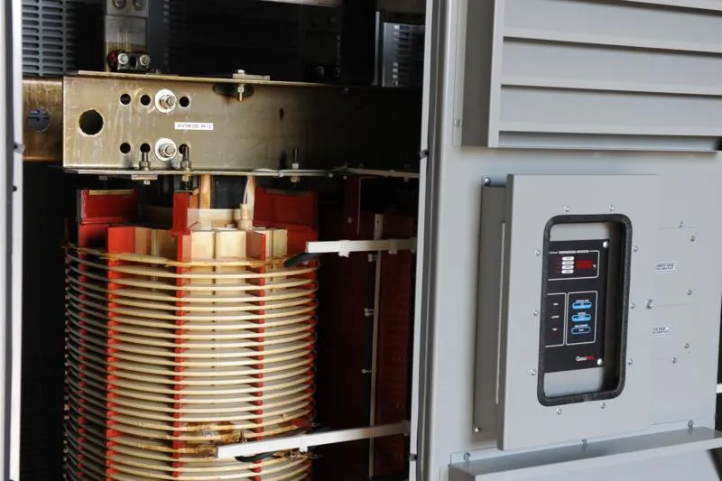 Industrial transformer with copper coil windings and red components inside metal enclosure with control panel