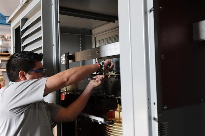 Technician adjusting internal components inside electrical transformer cabinet during maintenance