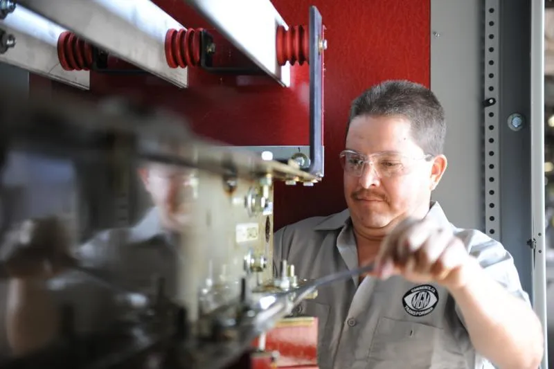 Technician inspecting high-voltage transformer equipment with red insulators in industrial facility