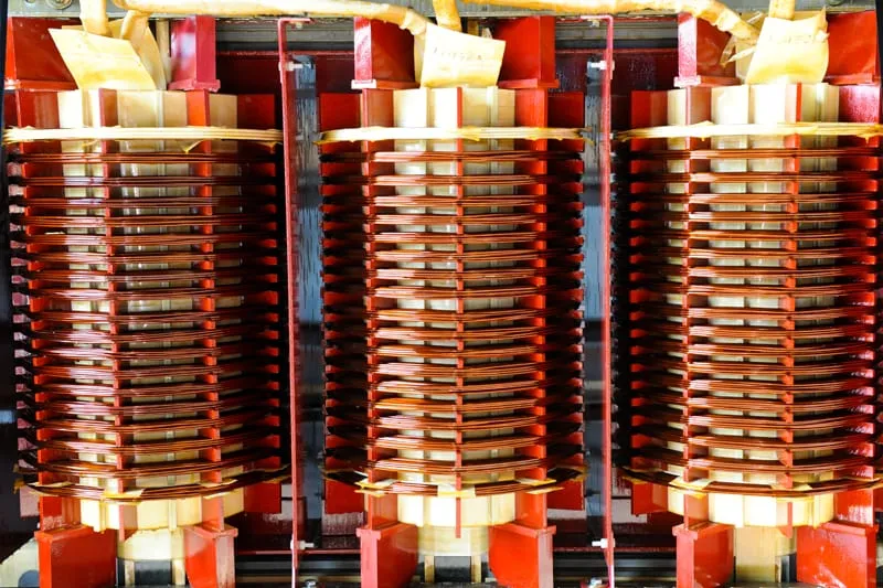 Three large electrical transformer coils with red and cream colored windings stacked vertically