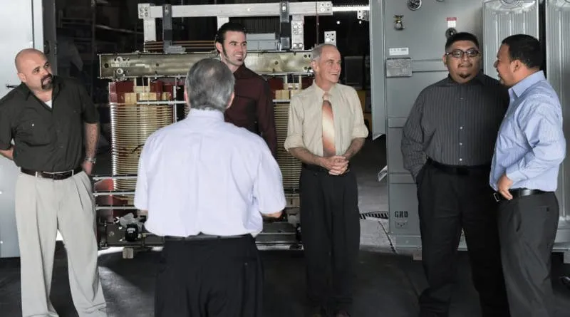 Group of professionals gathered around industrial transformer equipment during facility tour or training session