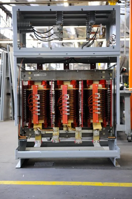 Industrial three-phase transformer with red coils and copper components in factory setting