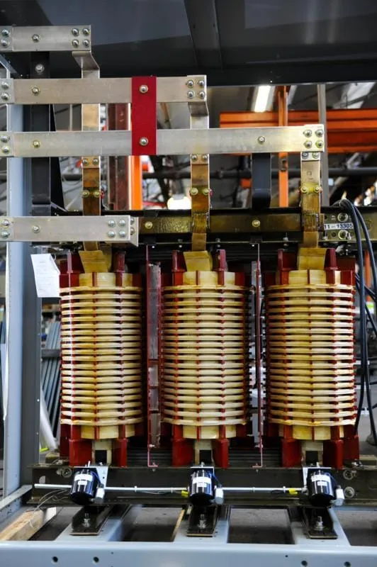 Three-phase industrial transformer with copper coils and red windings mounted in metal framework