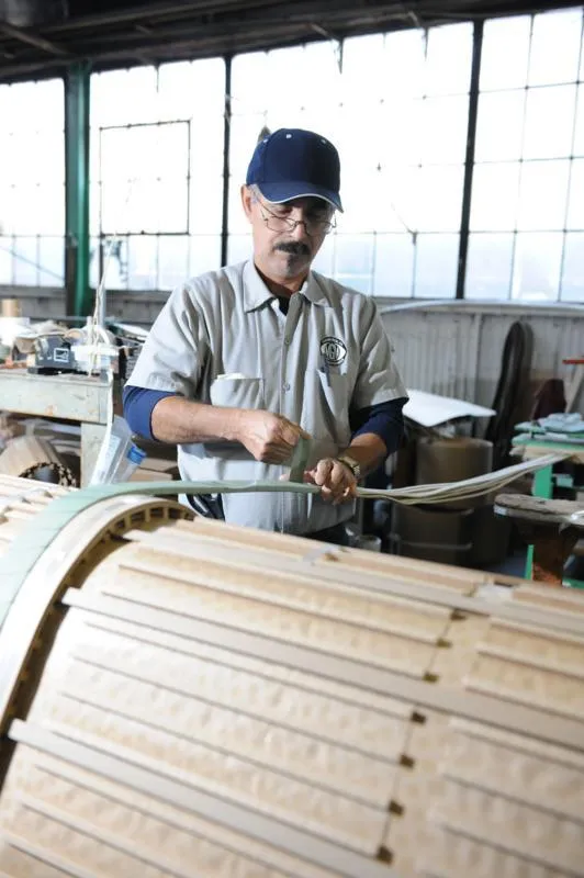 Craftsman working on curved wooden boat frame in workshop with large windows
