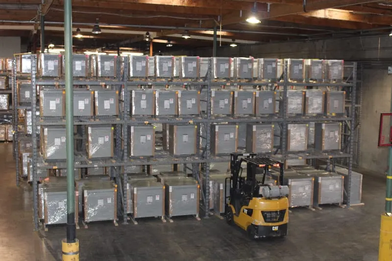 Warehouse storage with stacked transformers on industrial shelving and yellow forklift in foreground