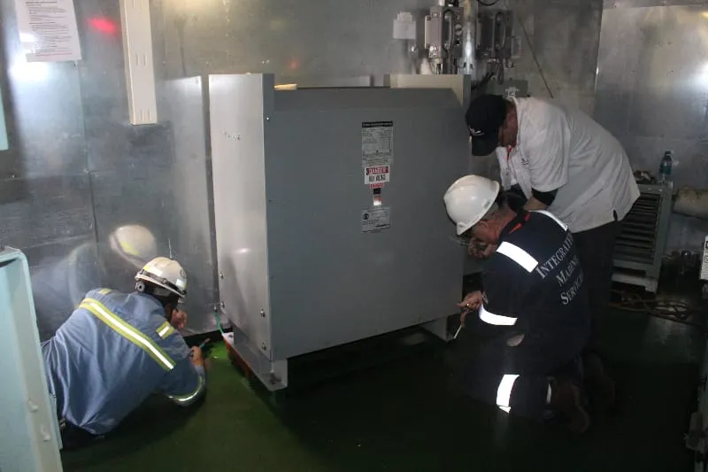 Technicians in safety gear installing large industrial transformer equipment in facility