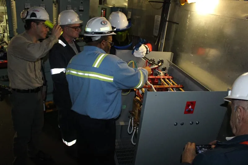 Industrial workers in hard hats performing electrical maintenance on transformer equipment in facility