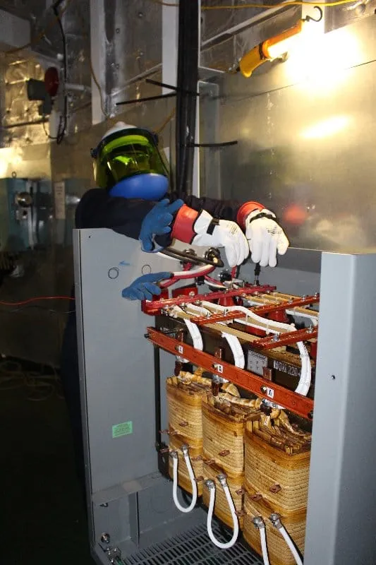Technician in safety gear inspecting industrial transformer coils and electrical components in MGM Transformers facility