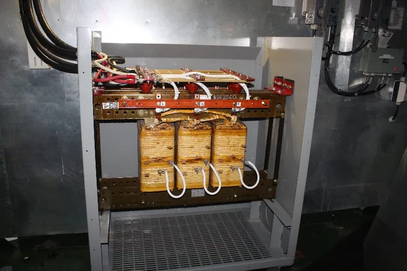 Industrial transformer with copper coils and golden windings mounted in metal enclosure