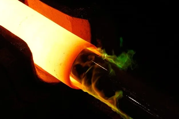 Glowing steel rod with orange and yellow heat, green sparks during industrial forging process for clean power applications