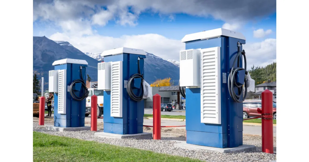 Three blue and white EV charging stations with red bollards in a mountainous landscape setting