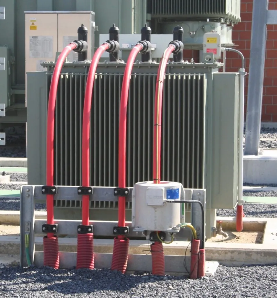 Large grounding transformer with red cables and radiator cooling fins installed at industrial facility