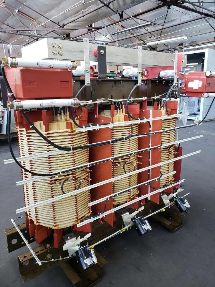 Industrial dry type transformer with red painted steel frame and copper coil windings in manufacturing facility
