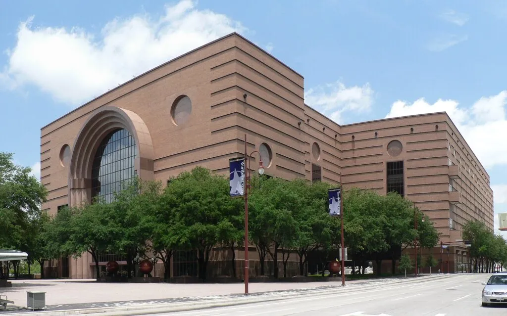 Wortham Theater exterior featuring Art Deco brick architecture with large arched window and green trees in Houston plaza