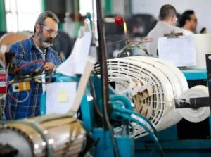 Factory worker in blue plaid shirt inspecting copper conductor coils on manufacturing equipment in industrial workshop