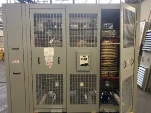 Large industrial custom transformer with metal mesh doors and ventilation panels in factory setting